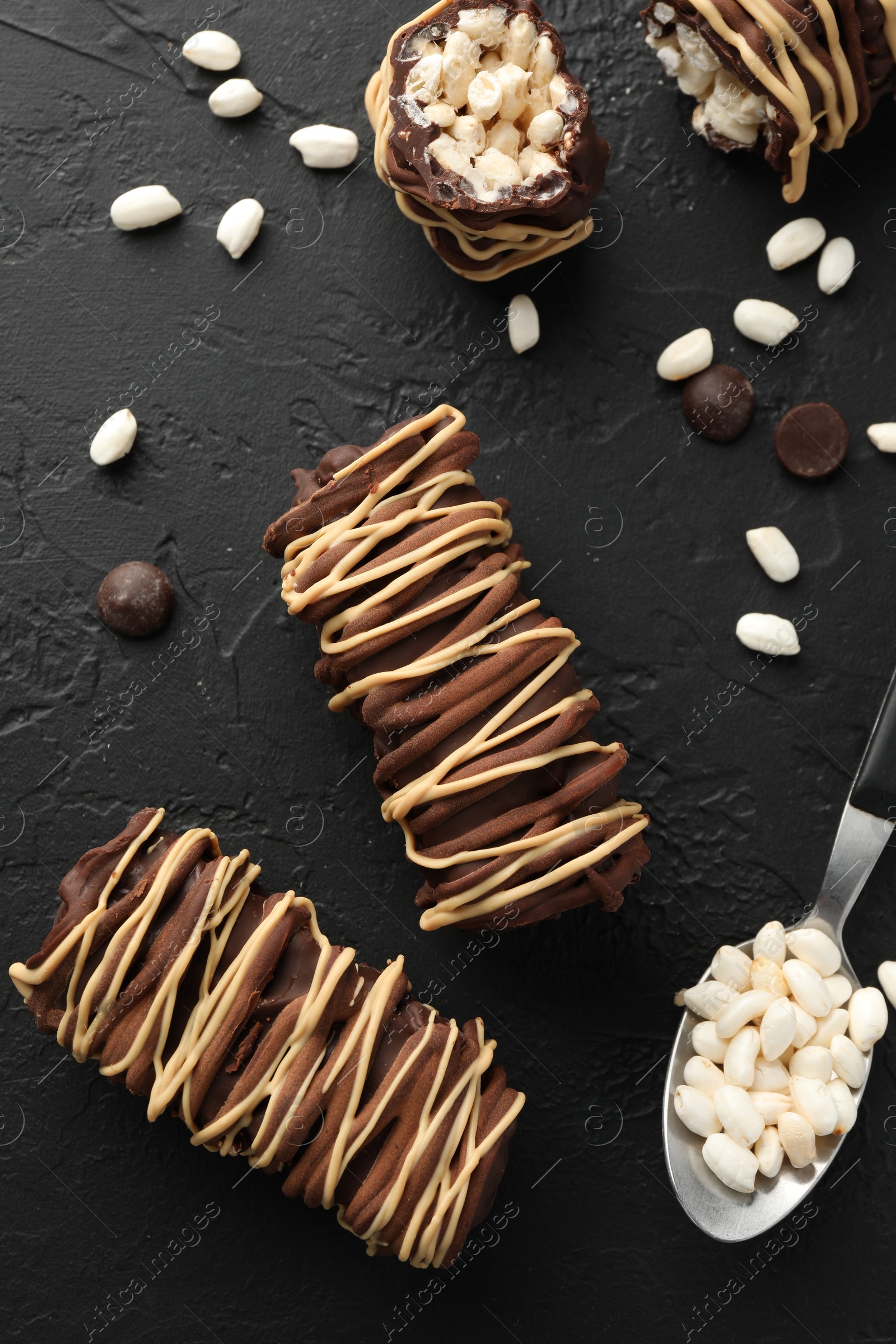 Photo of Delicious chocolate puffed rice bars and spoon on dark gray textured table, flat lay