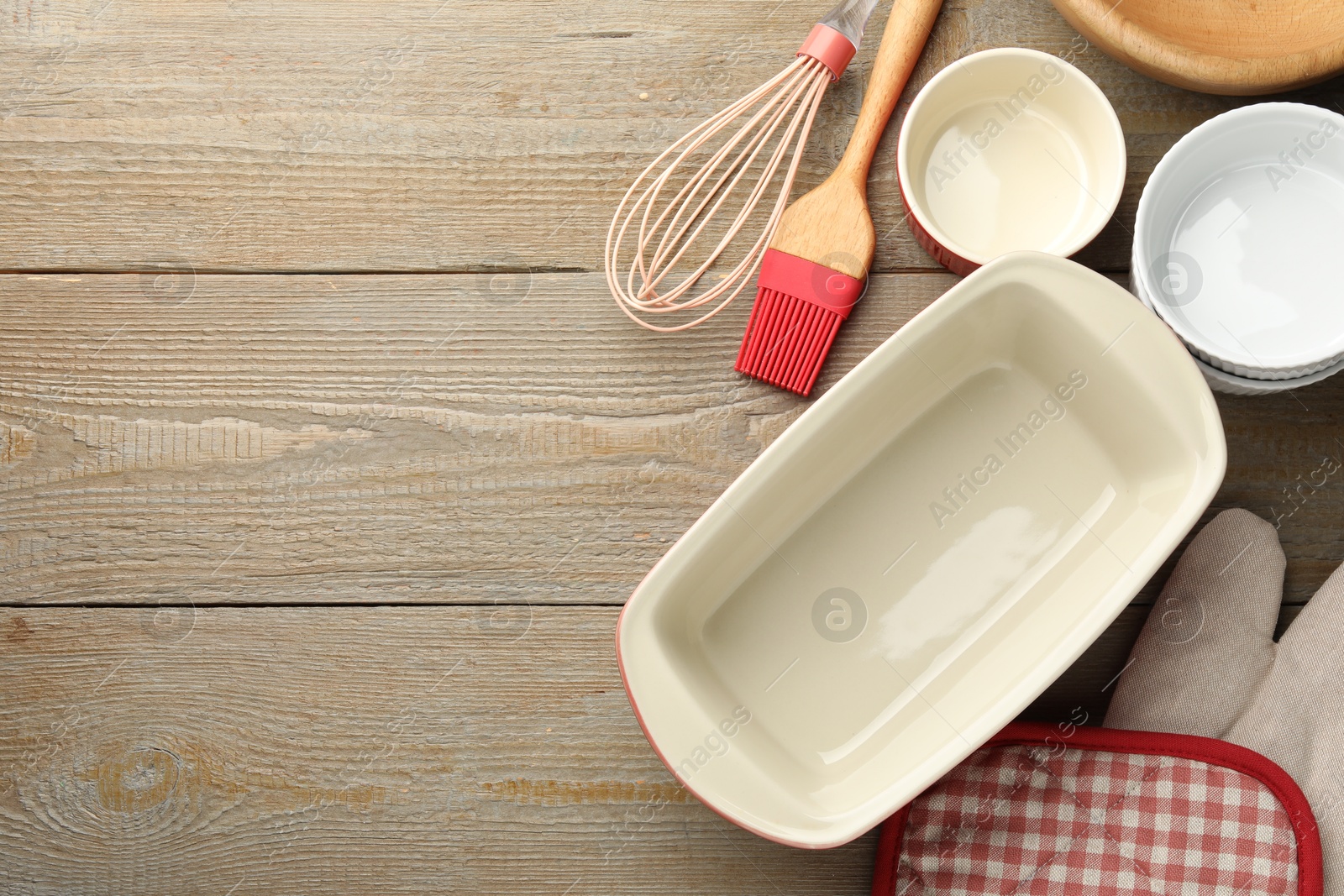 Photo of Ceramic casseroles and other cooking utensils on wooden table, flat lay. Space for text