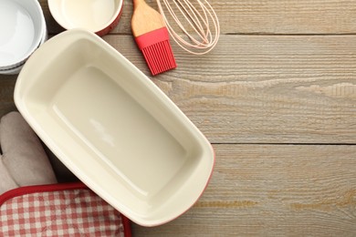 Photo of Ceramic casseroles and other cooking utensils on wooden table, flat lay. Space for text