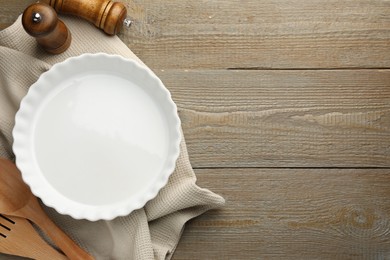 Photo of Ceramic casserole and other cooking utensils on wooden table, flat lay. Space for text