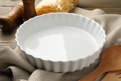 Photo of Ceramic casserole and other cooking utensils on wooden table, closeup