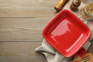 Photo of Ceramic casserole, raw pasta, shakers, brush and slotted turner on wooden table, flat lay. Space for text