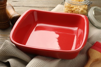 Photo of Ceramic casserole, raw pasta, shakers and brush on wooden table, closeup