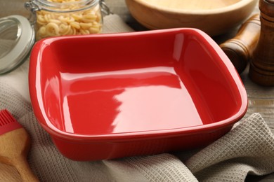 Photo of Ceramic casserole, raw pasta, shakers and brush on table, closeup