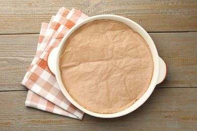 Photo of Ceramic casserole with baking parchment paper on wooden table, top view