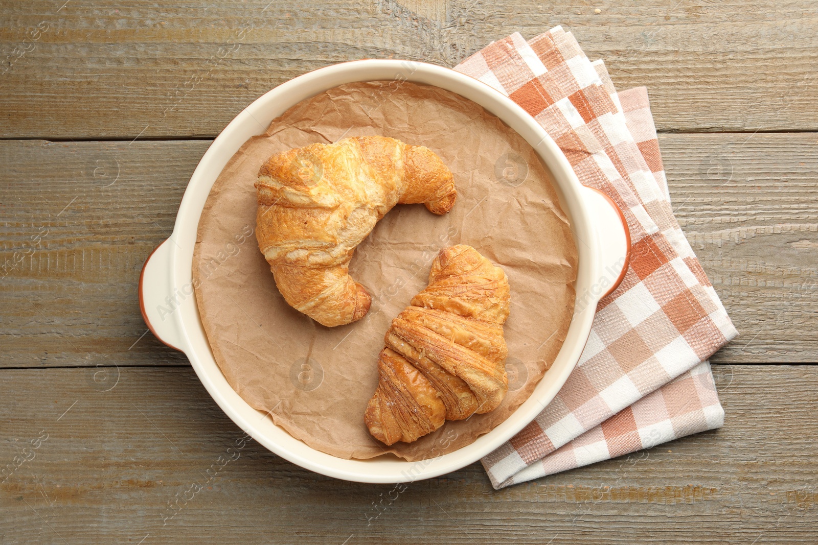 Photo of Ceramic casserole with croissants and baking parchment paper on wooden table, top view