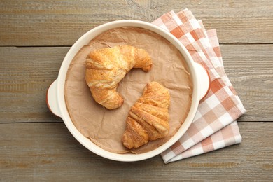 Photo of Ceramic casserole with croissants and baking parchment paper on wooden table, top view