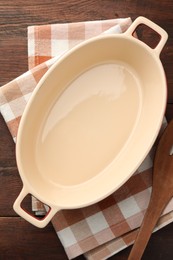 Photo of Ceramic casserole and slotted turner on wooden table, top view