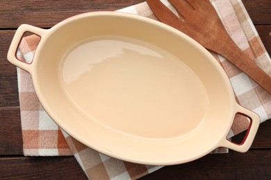 Photo of Ceramic casserole and slotted turner on wooden table, top view