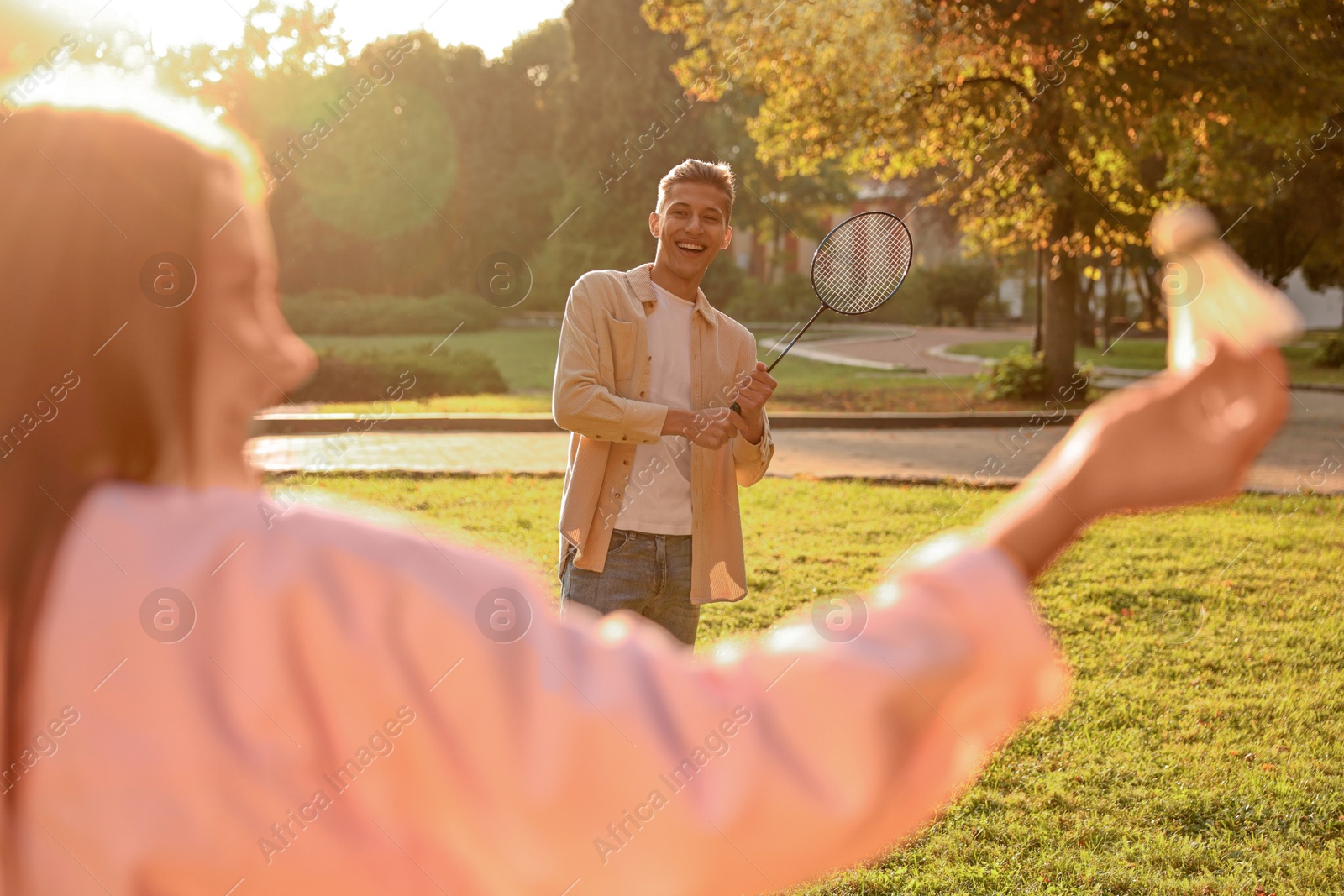 Photo of Young woman and man playing badminton in park on sunny day, selective focus