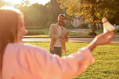 Photo of Young woman and man playing badminton in park on sunny day, selective focus