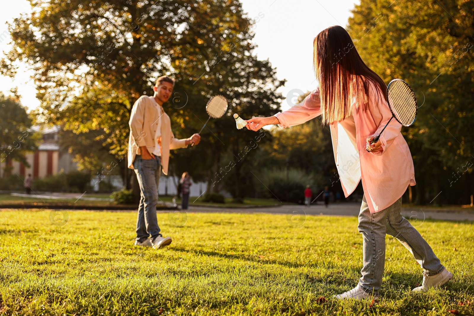 Photo of Young woman and man playing badminton in park on sunny day, selective focus