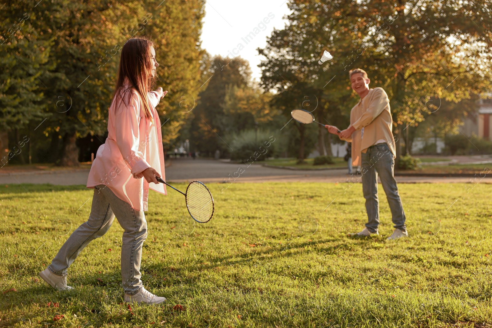 Photo of Young woman and man playing badminton in park on sunny day, selective focus