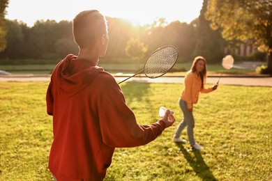 Photo of Young man and woman playing badminton in park on sunny day, selective focus