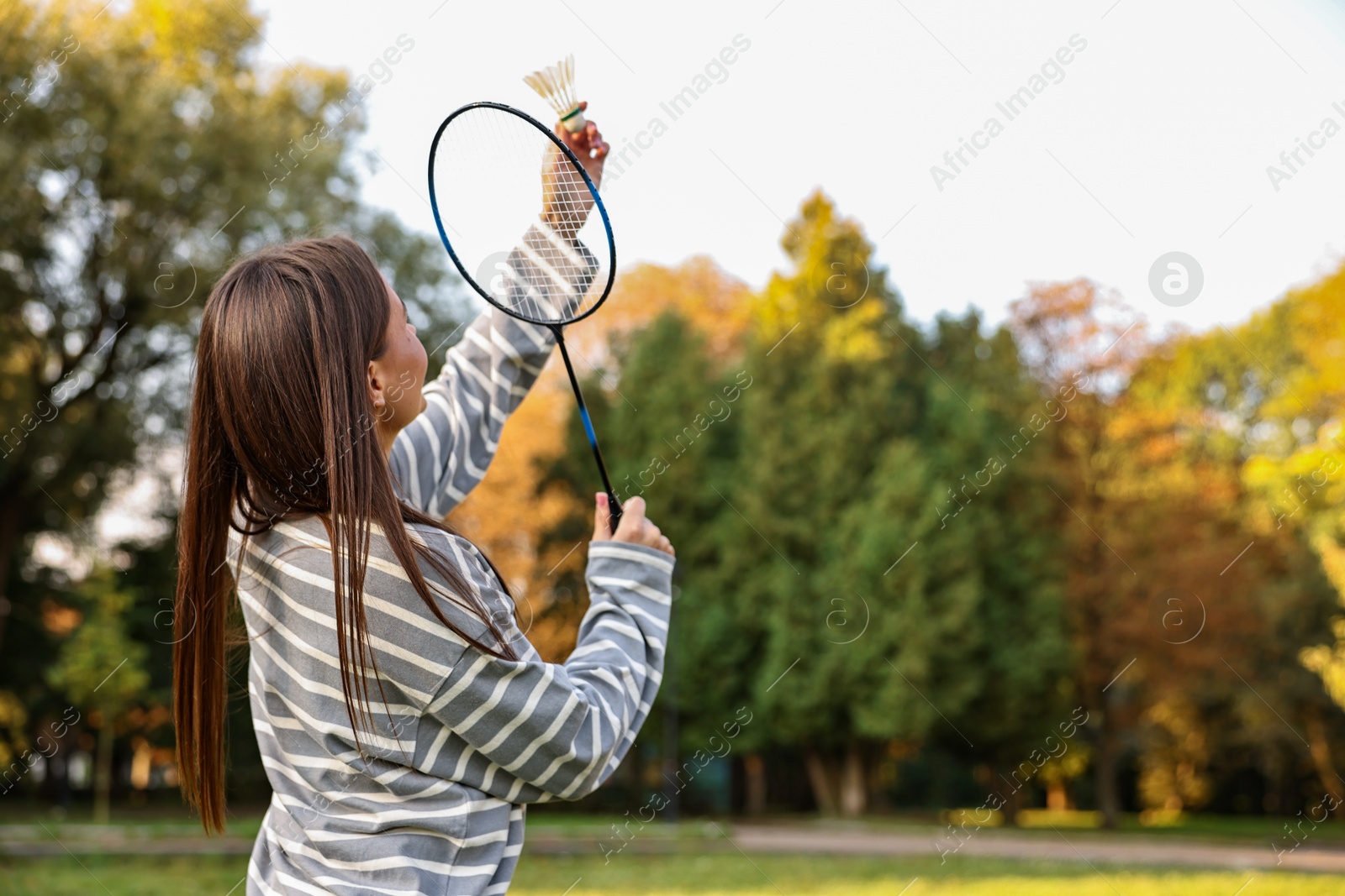 Photo of Young woman with badminton racket and shuttlecock in park, low angle view. Space for text