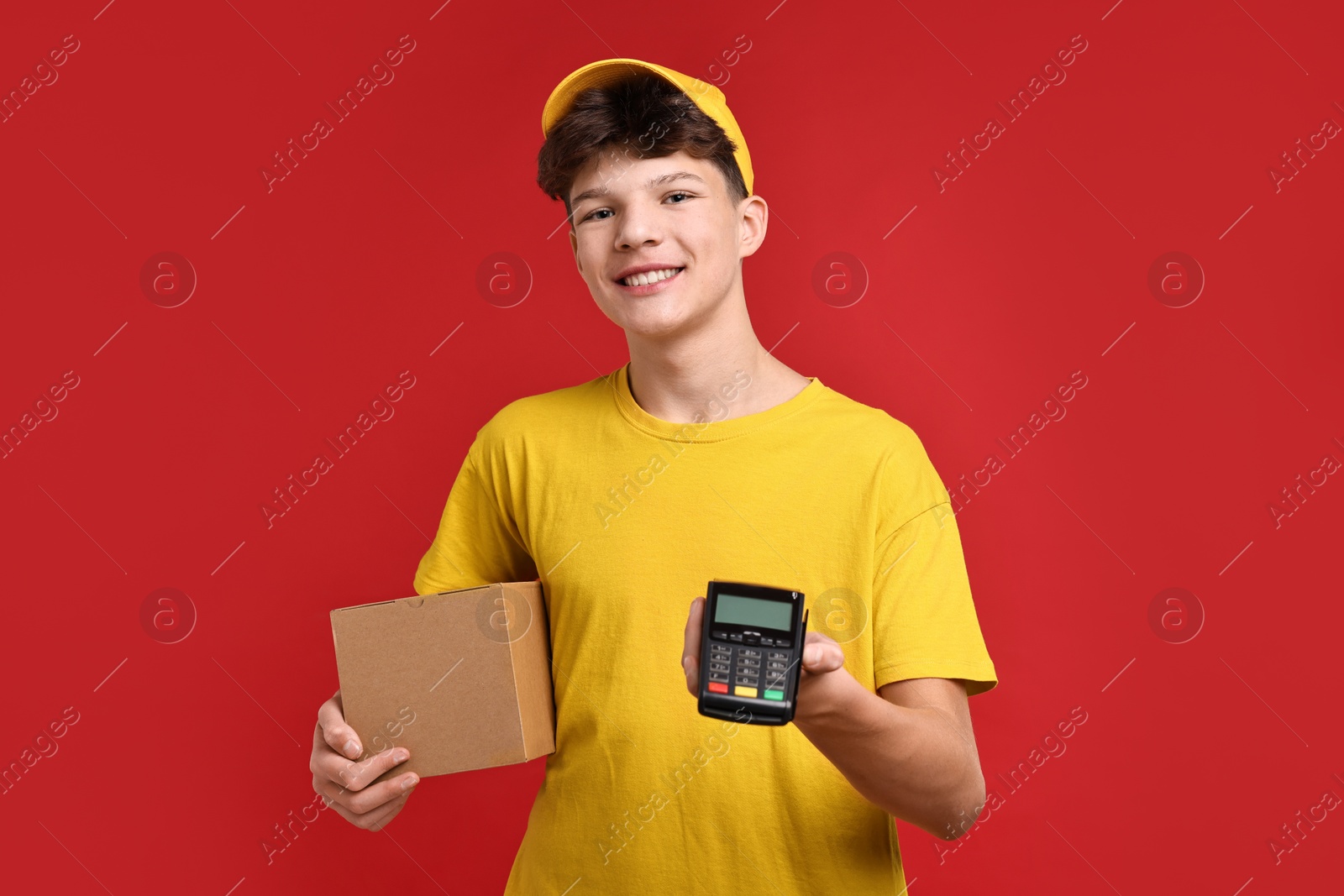 Photo of Teenage boy with parcel and payment terminal working as courier on red background