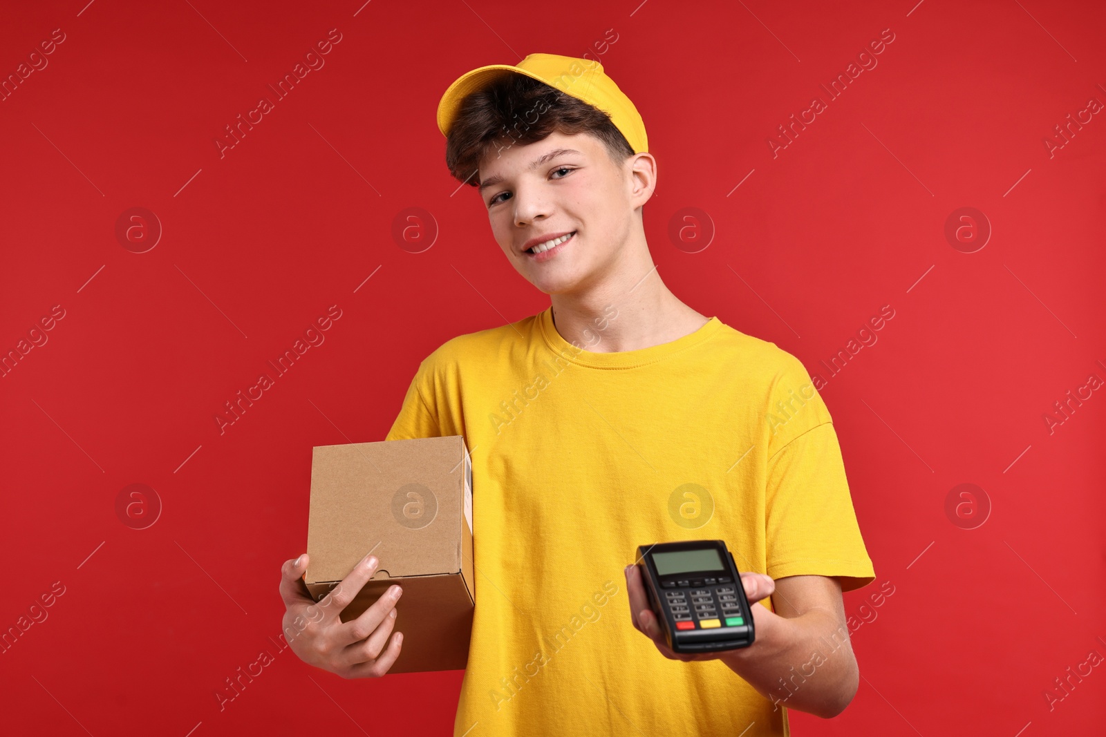 Photo of Teenage boy with parcel and payment terminal working as courier on red background