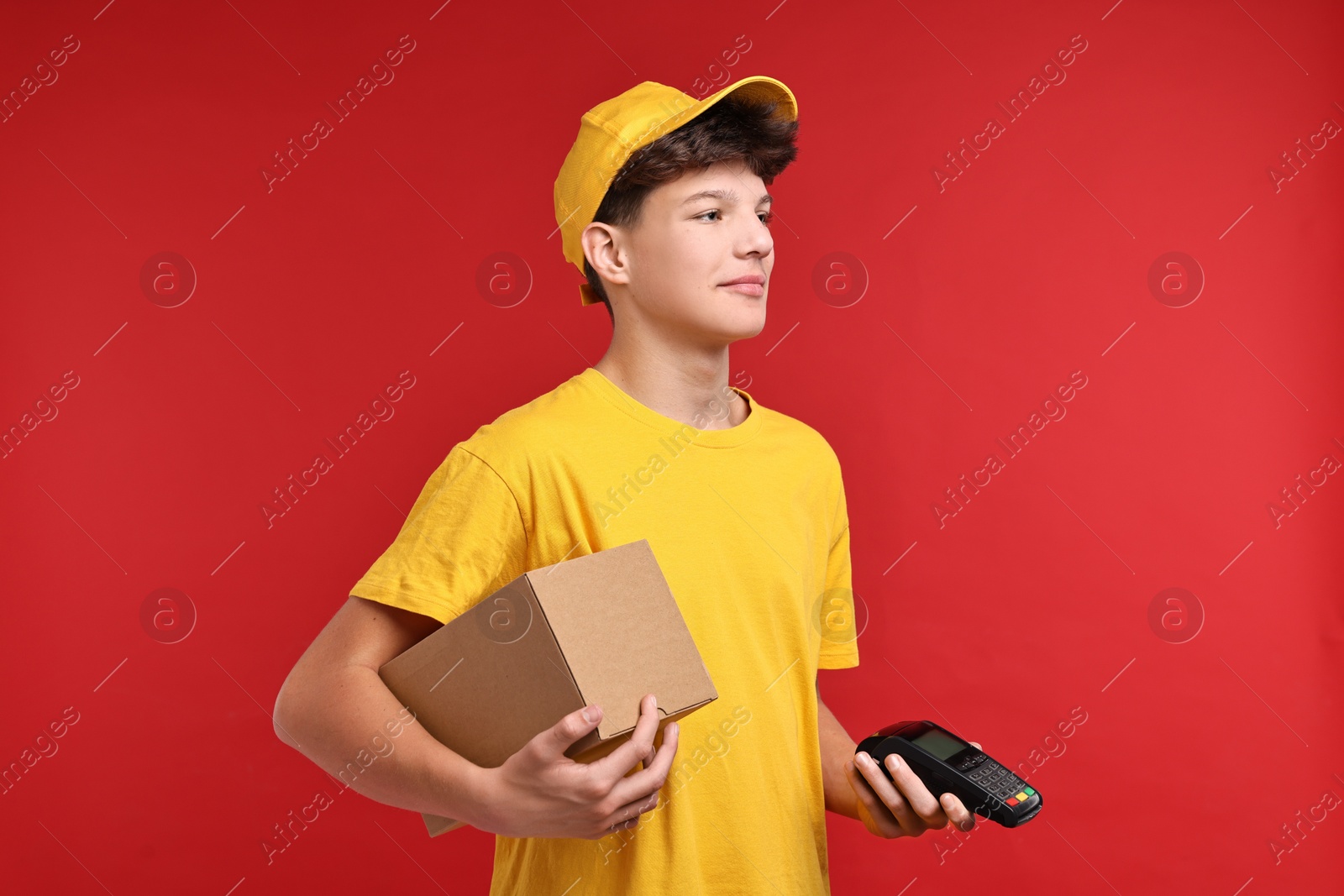 Photo of Teenage boy with parcel and payment terminal working as courier on red background