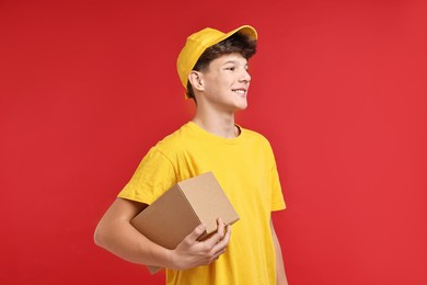 Photo of Teenage boy with parcel working as courier on red background