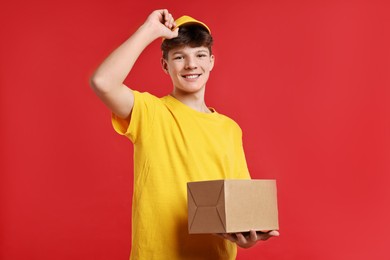 Photo of Teenage boy with parcel working as courier on red background