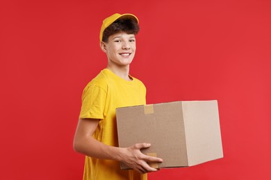 Photo of Teenage boy with parcel working as courier on red background