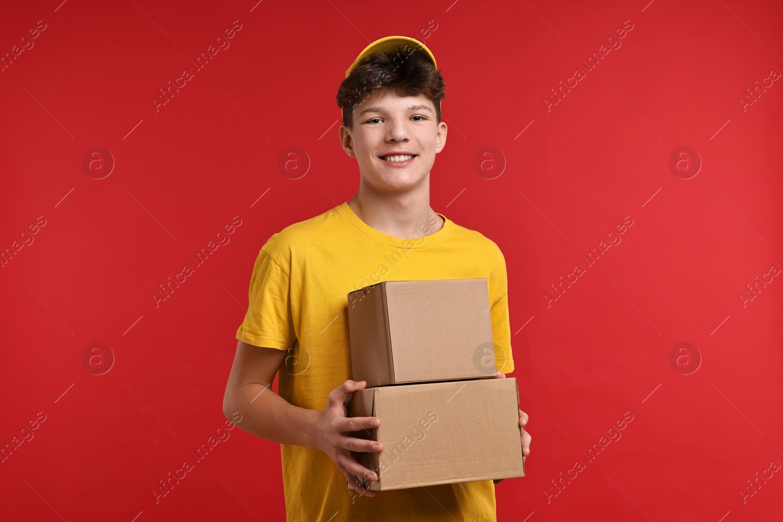 Photo of Teenage boy with parcels working as courier on red background