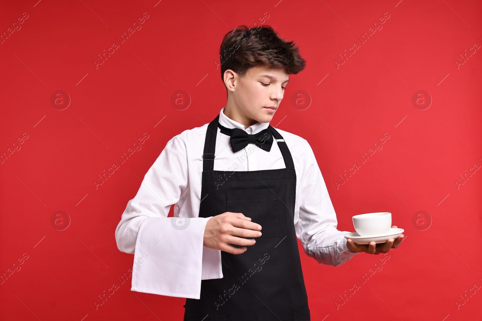 Photo of Teenage boy with cup of drink working as waiter on red background