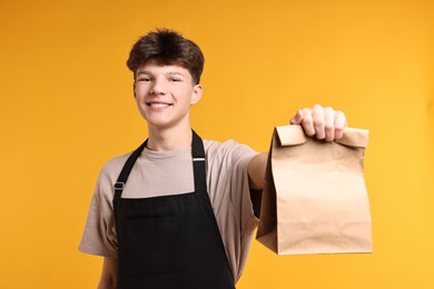 Photo of Teenage boy with paper bag working as cashier on orange background