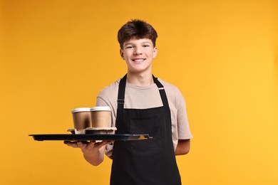 Photo of Teenage boy with order working as waiter on orange background