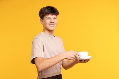 Photo of Teenage boy with cup working as barista on orange background