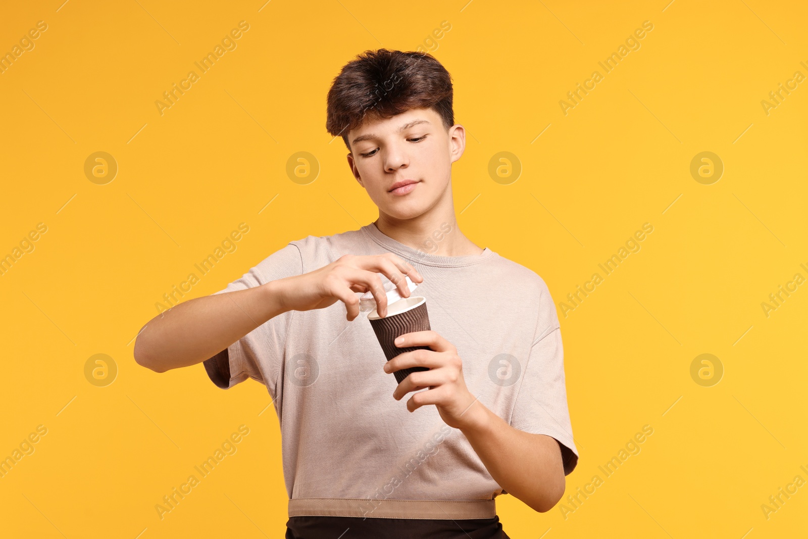 Photo of Teenage boy with paper cup working as barista on orange background