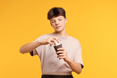 Photo of Teenage boy with paper cup working as barista on orange background