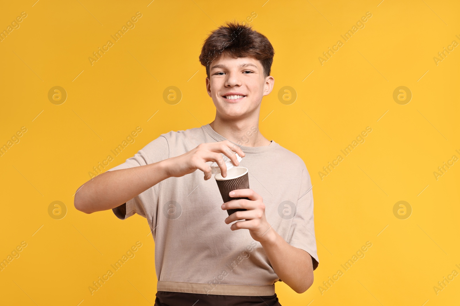 Photo of Teenage boy with paper cup working as barista on orange background