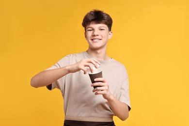 Photo of Teenage boy with paper cup working as barista on orange background