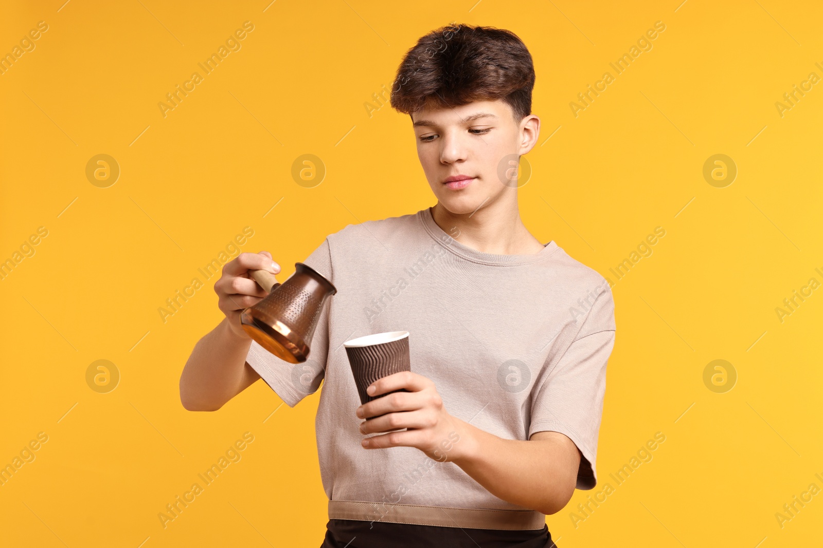 Photo of Teenage boy with cezve pot and paper cup working as barista on orange background