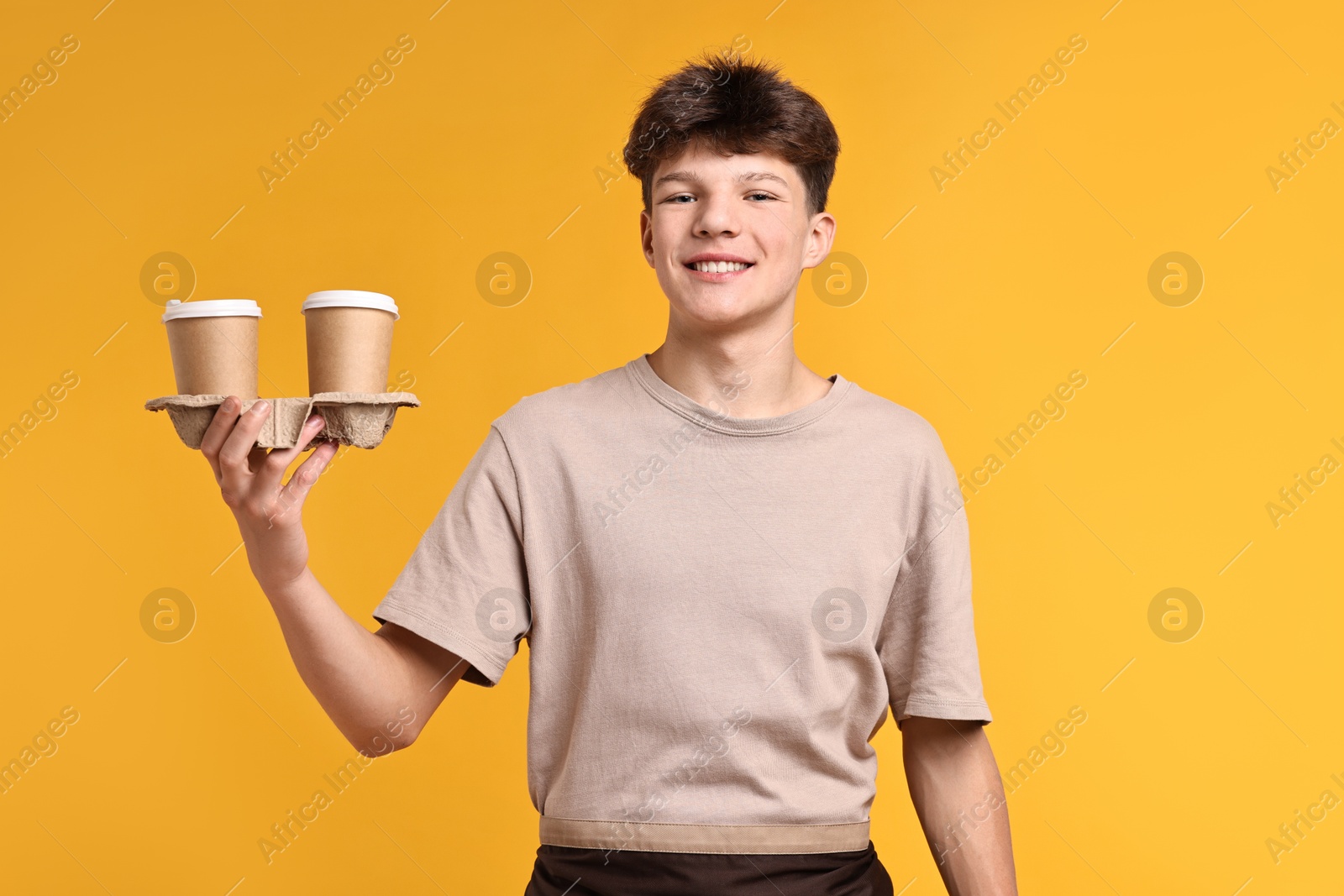 Photo of Teenage boy with paper cups working as barista on orange background