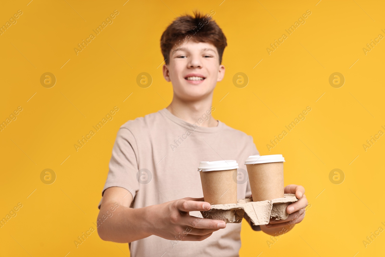 Photo of Teenage boy with paper cups working as barista on orange background