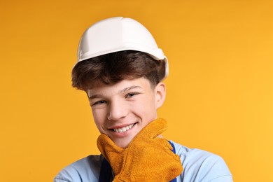 Photo of Teenage boy in hardhat working as builder on orange background