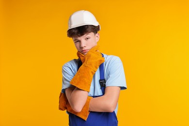 Photo of Teenage boy in hardhat working as builder on orange background