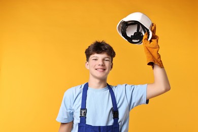 Photo of Teenage boy in hardhat working as builder on orange background