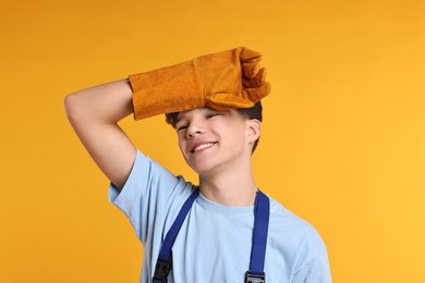 Photo of Teenage boy in protective gloves working as builder on orange background