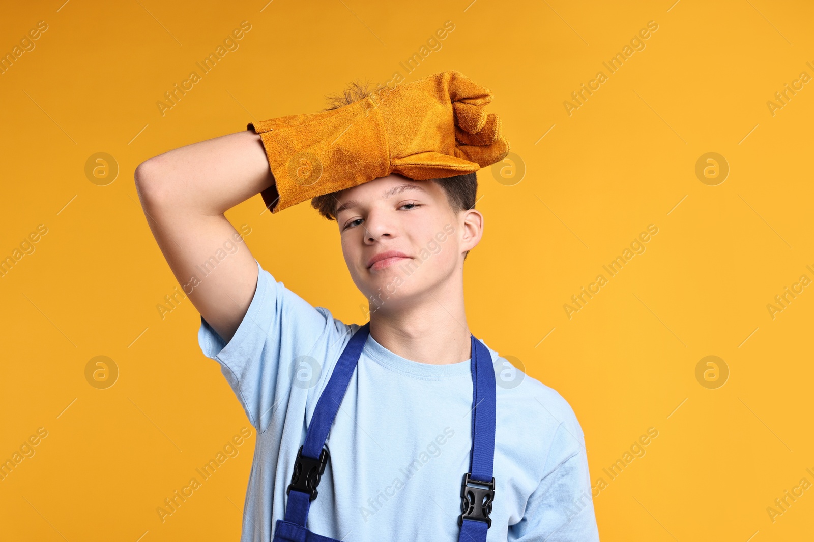 Photo of Teenage boy in protective gloves working as builder on orange background