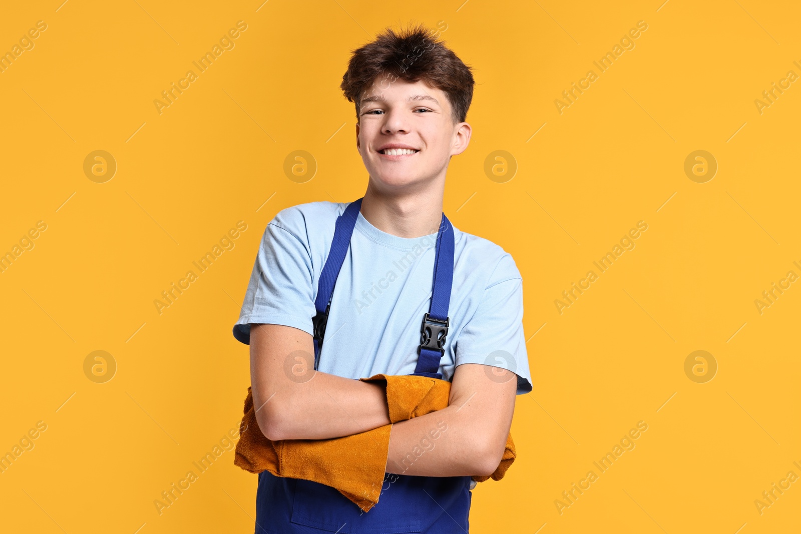 Photo of Teenage boy in protective gloves working as builder on orange background