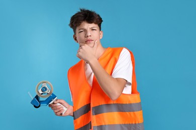 Photo of Teenage boy with tape gun dispenser in safety vest working as warehouse packer on blue background