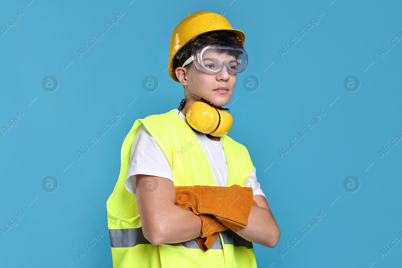 Photo of Teenage boy in hardhat, protective mask and safety vest working as builder on blue background