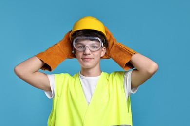 Photo of Teenage boy in hardhat, protective mask and safety vest working as builder on blue background