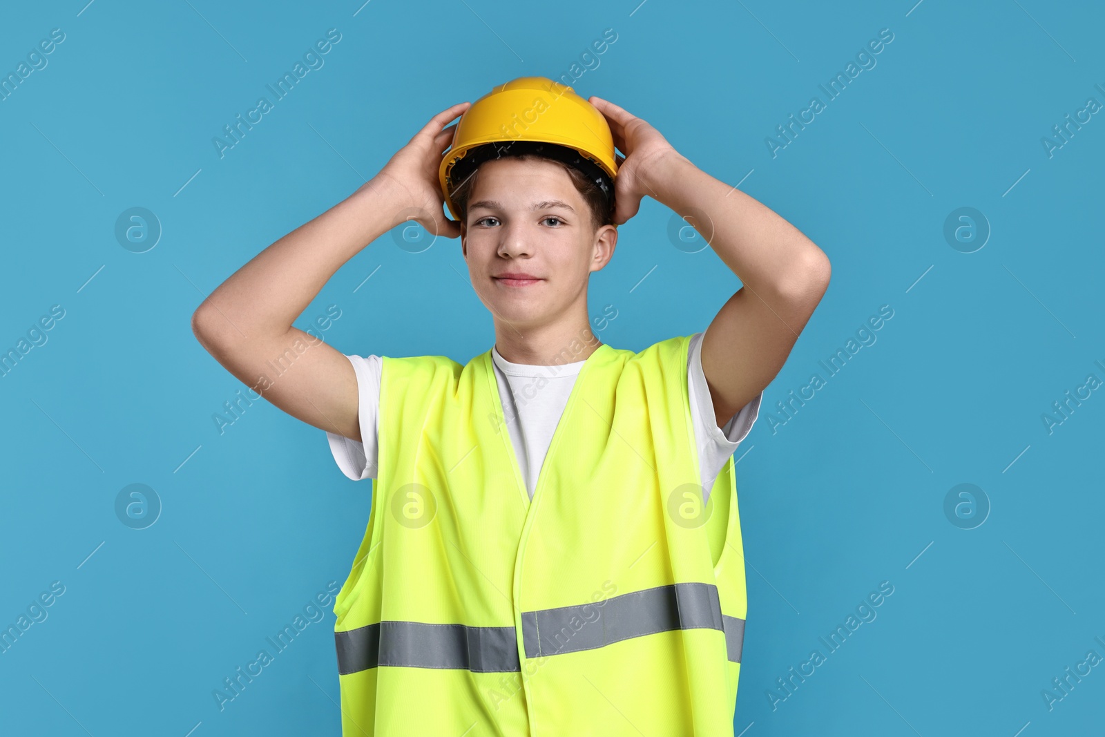 Photo of Teenage boy in hardhat and safety vest working as builder on blue background