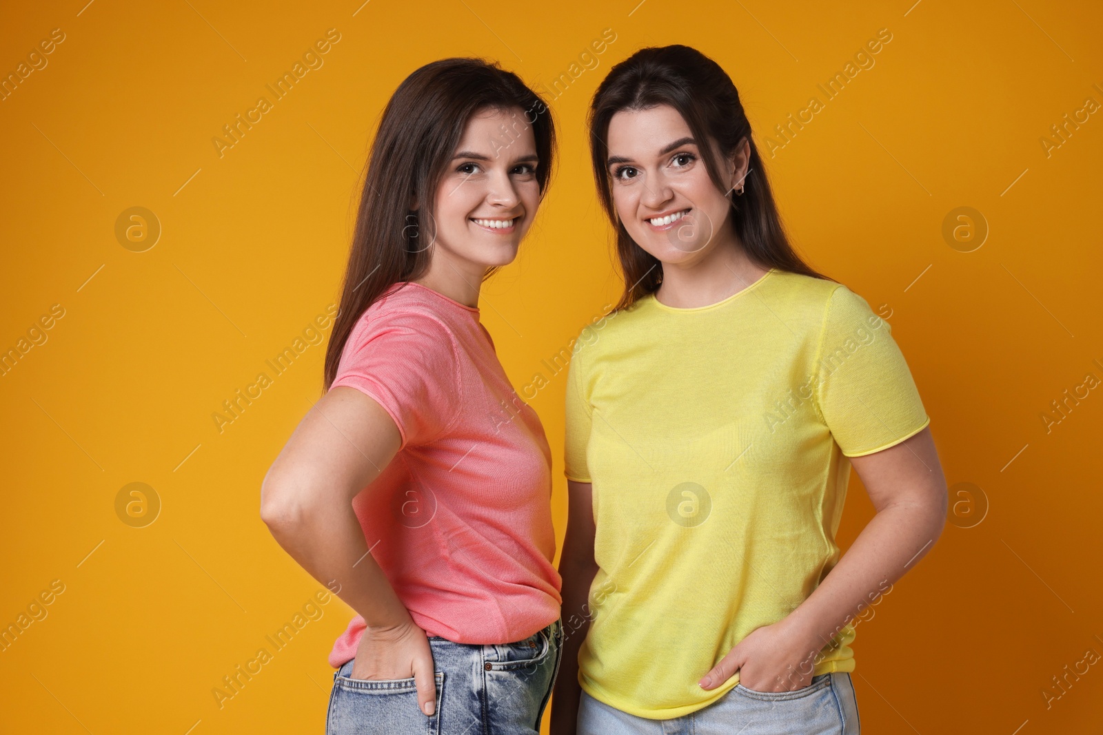 Photo of Portrait of happy twin sisters on orange background