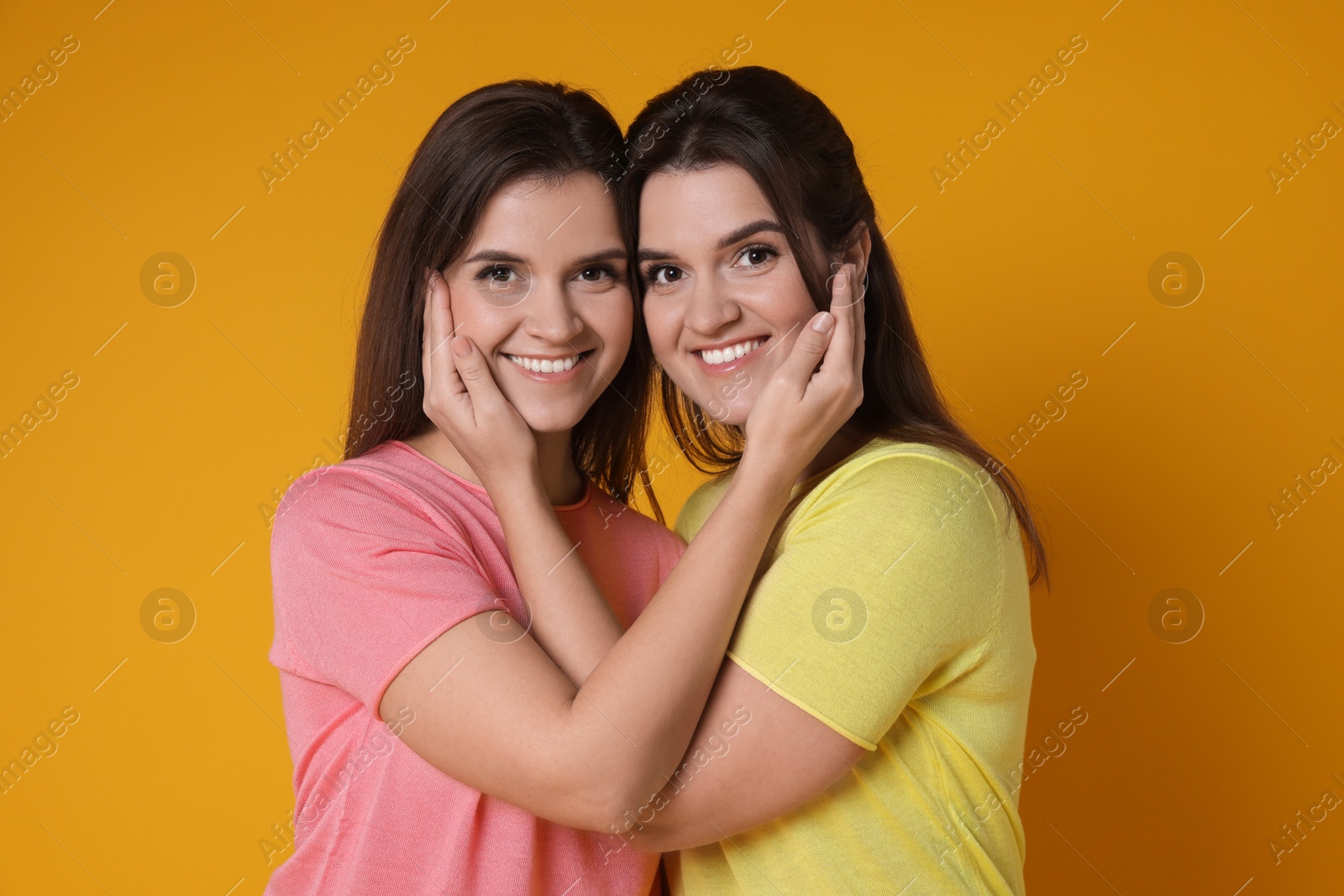 Photo of Portrait of happy twin sisters on orange background