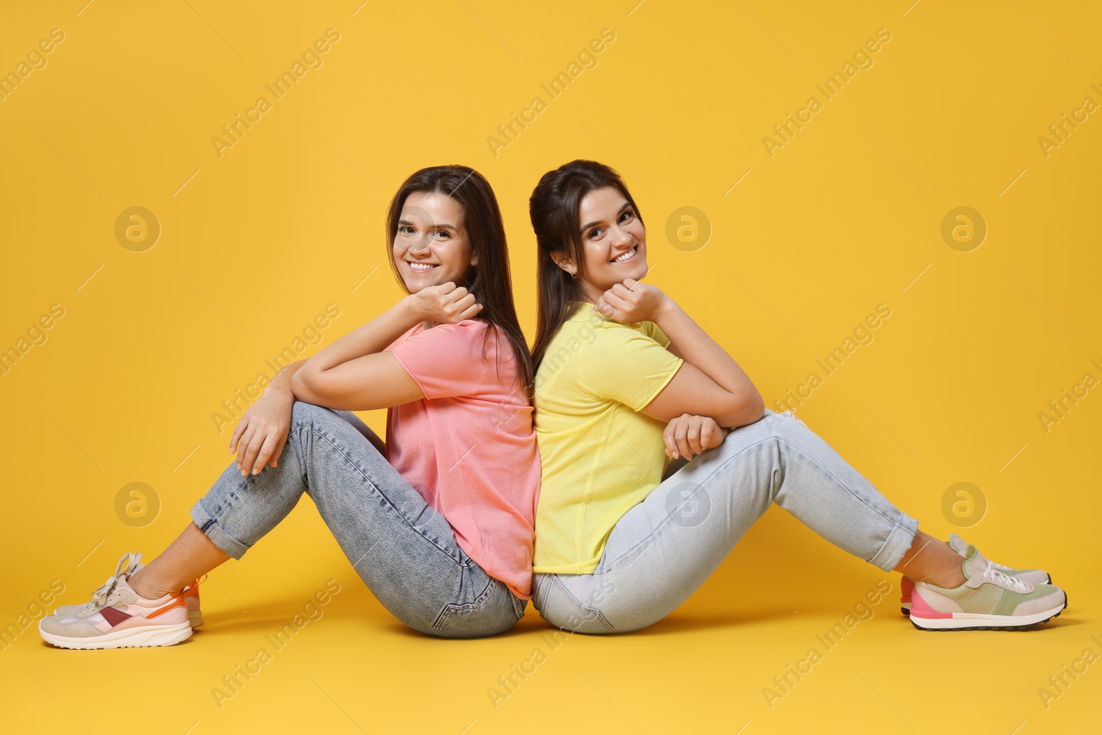 Photo of Portrait of happy twin sisters on orange background